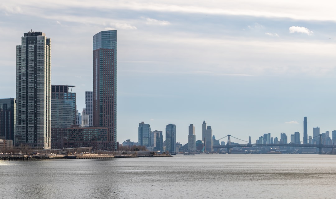 Modern skyscrapers by the water under a cloudy sky.